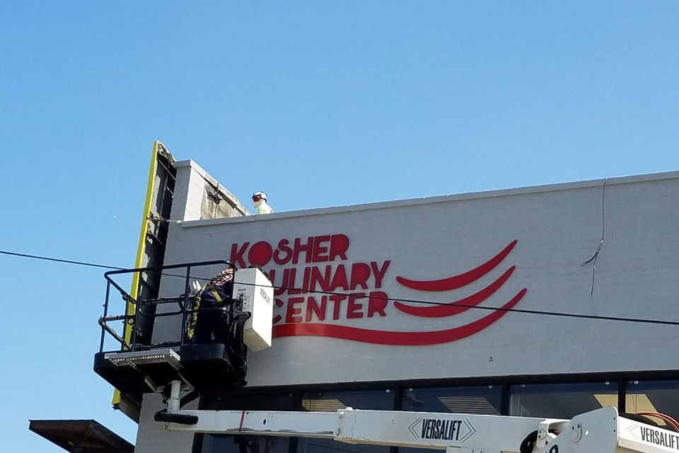 Red dimensional letters and a red swoosh logo being installed on a building parapet from a bucket truck