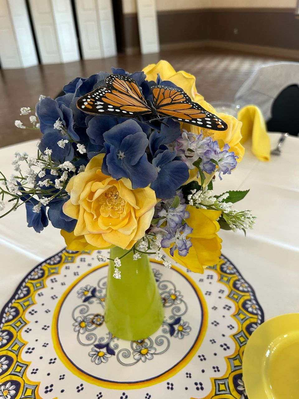 Blue and yellow flower arrangement featuring a butterfly centerpiece on a decorated table.