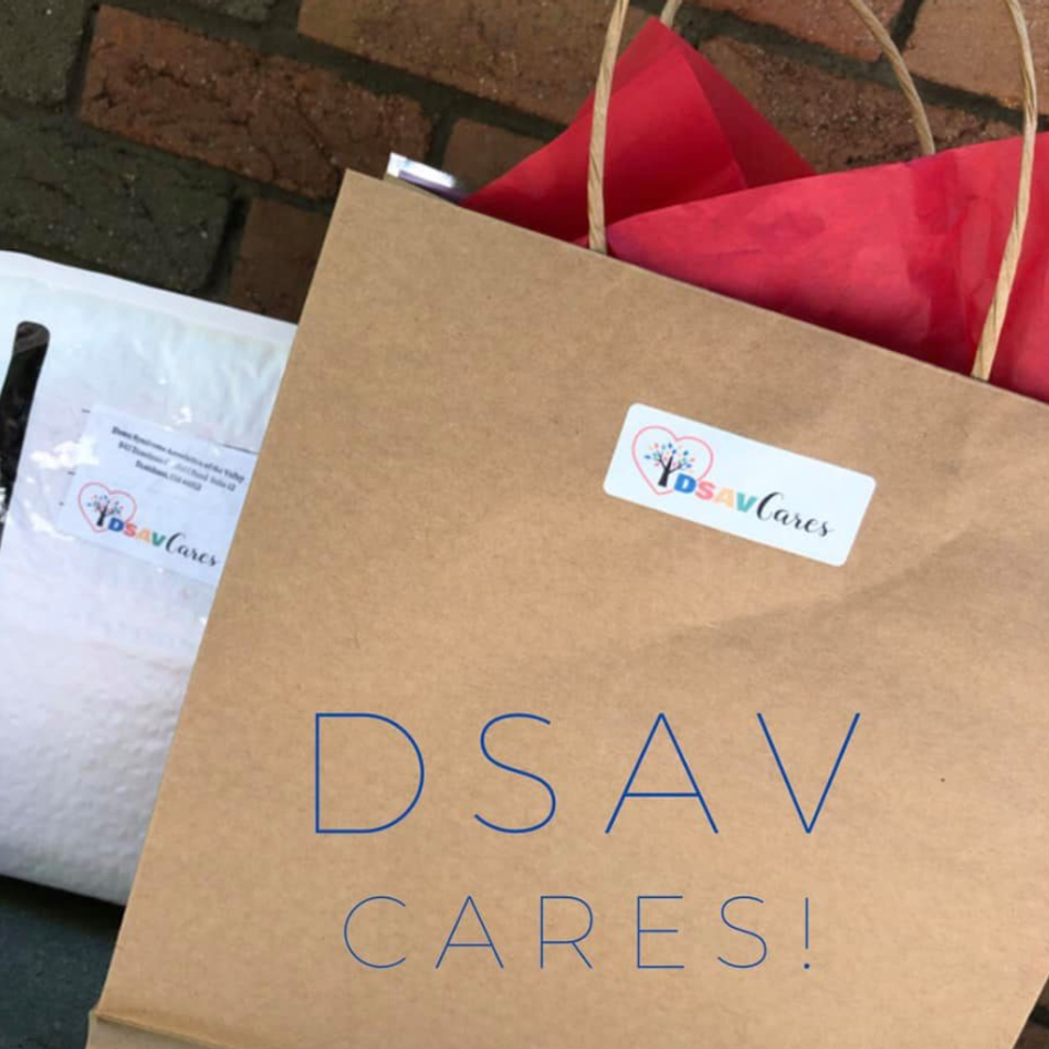 A DSAV Cares gift bag with red tissue paper and a DSAV Cares logo sticker, prepared as a care package for an individual with Down syndrome or their family.
