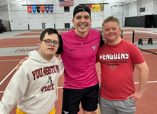 Two participants with Down syndrome posing with a Youngstown State tennis athlete during an adaptive tennis program.