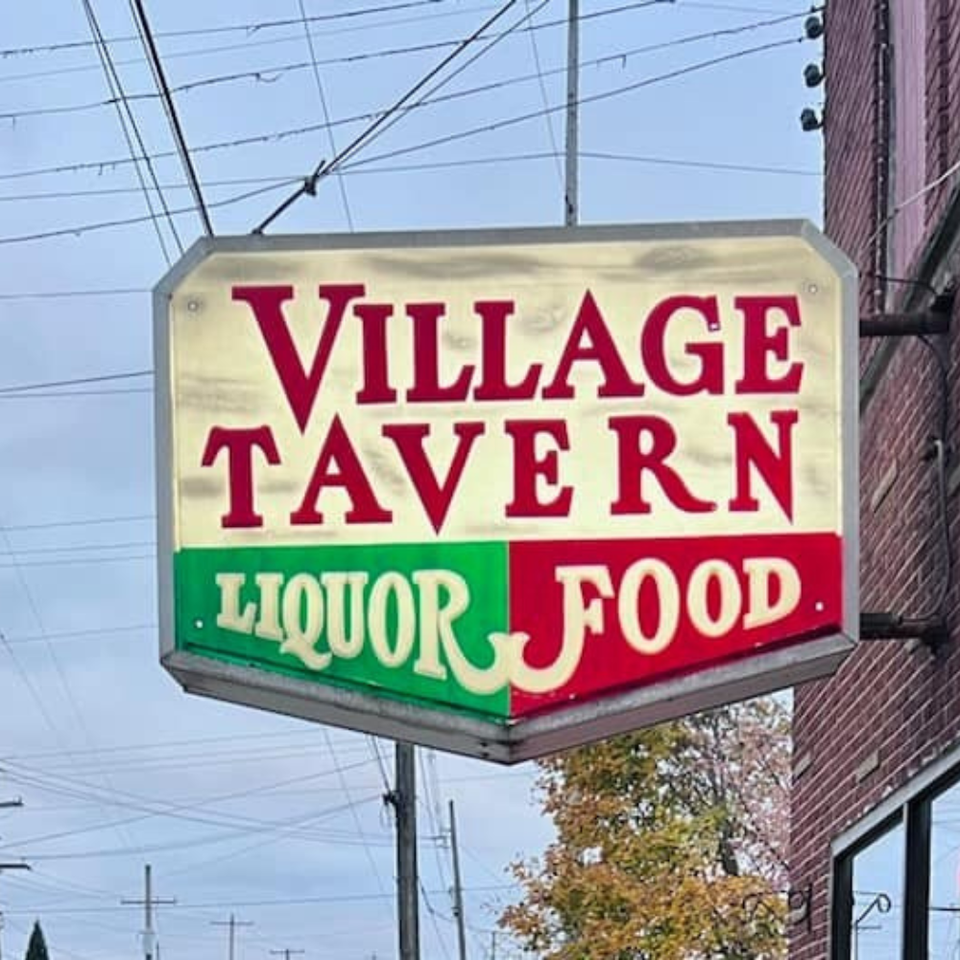 Close-up of Village Tavern sign reading “Liquor Food” mounted on brick building