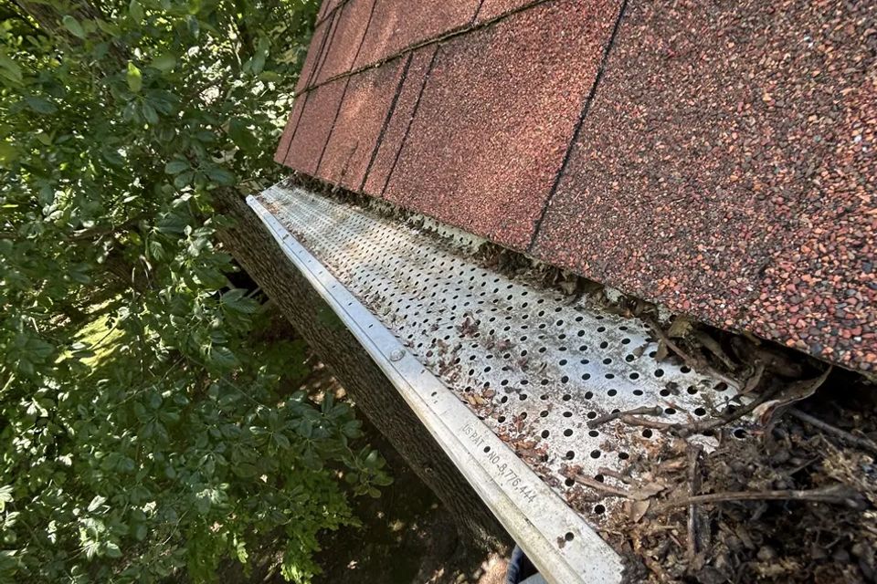 Debris-filled gutter with mesh guard along red shingle roof after gutter cleaning in Harrisburg PA