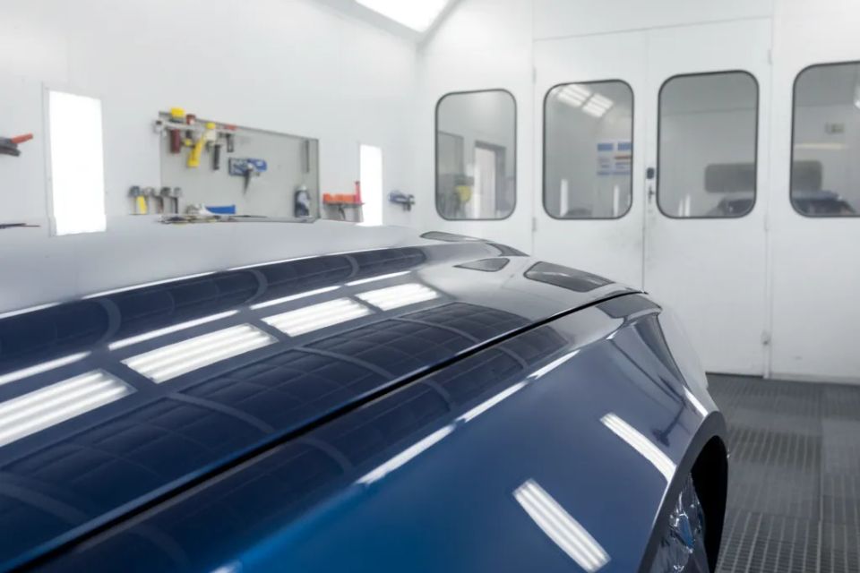 Close up of a freshly painted, flawless blue car hood inside a professional, bright white paint booth with LED lighting