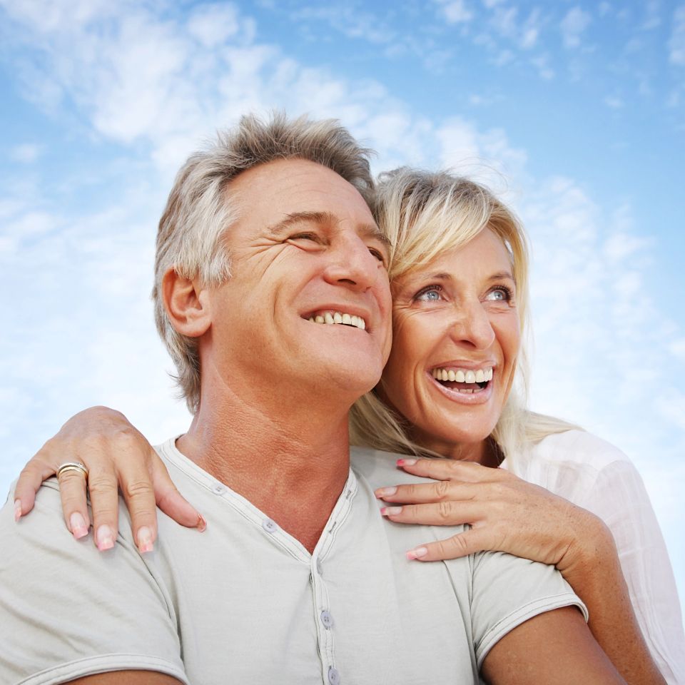 Smiling mature couple embracing outdoors under a blue sky after Myers Cocktail IV therapy in Palm Beach County FL