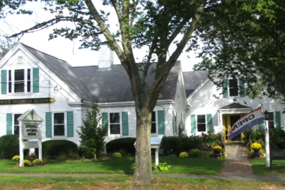 Older colonial building with green shutters, with a open flag