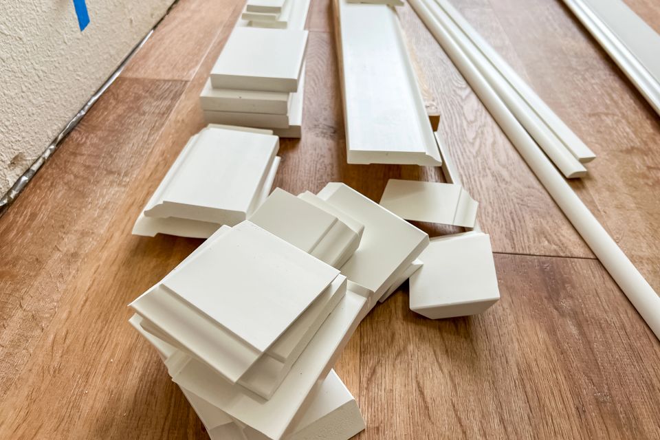 Freshly cut white baseboard and trim pieces stacked on new vinyl plank flooring