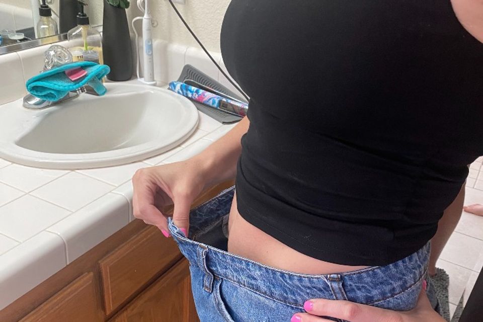 Image of a client showing weight loss by showing how big her shorts are now, she is holding the front of the shorts