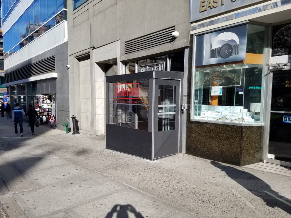 Compact dark grey vestibule with a clear glass door enclosing a single storefront entrance on a New York City sidewalk