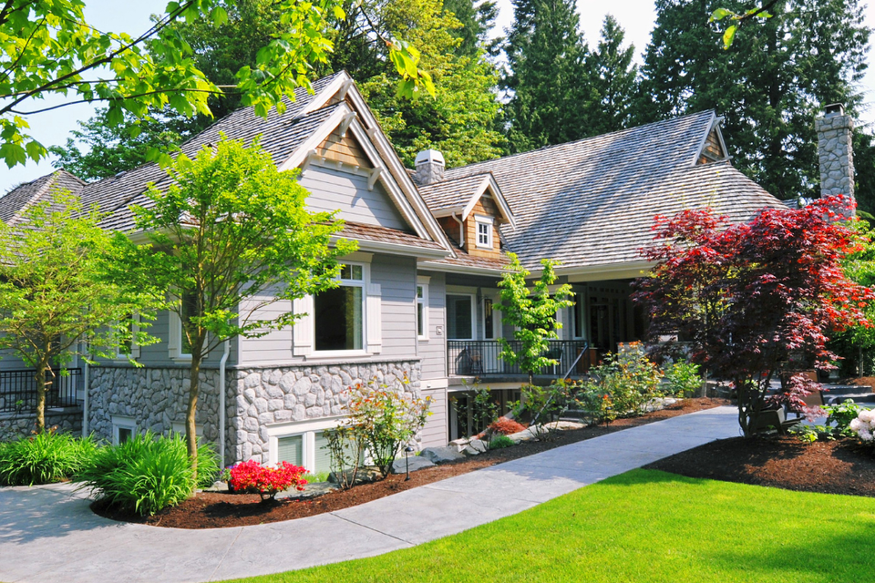 Beautiful residential landscape featuring a lush green lawn, curved concrete walkway, ornamental trees, colorful flower beds, and professionally maintained landscaping.