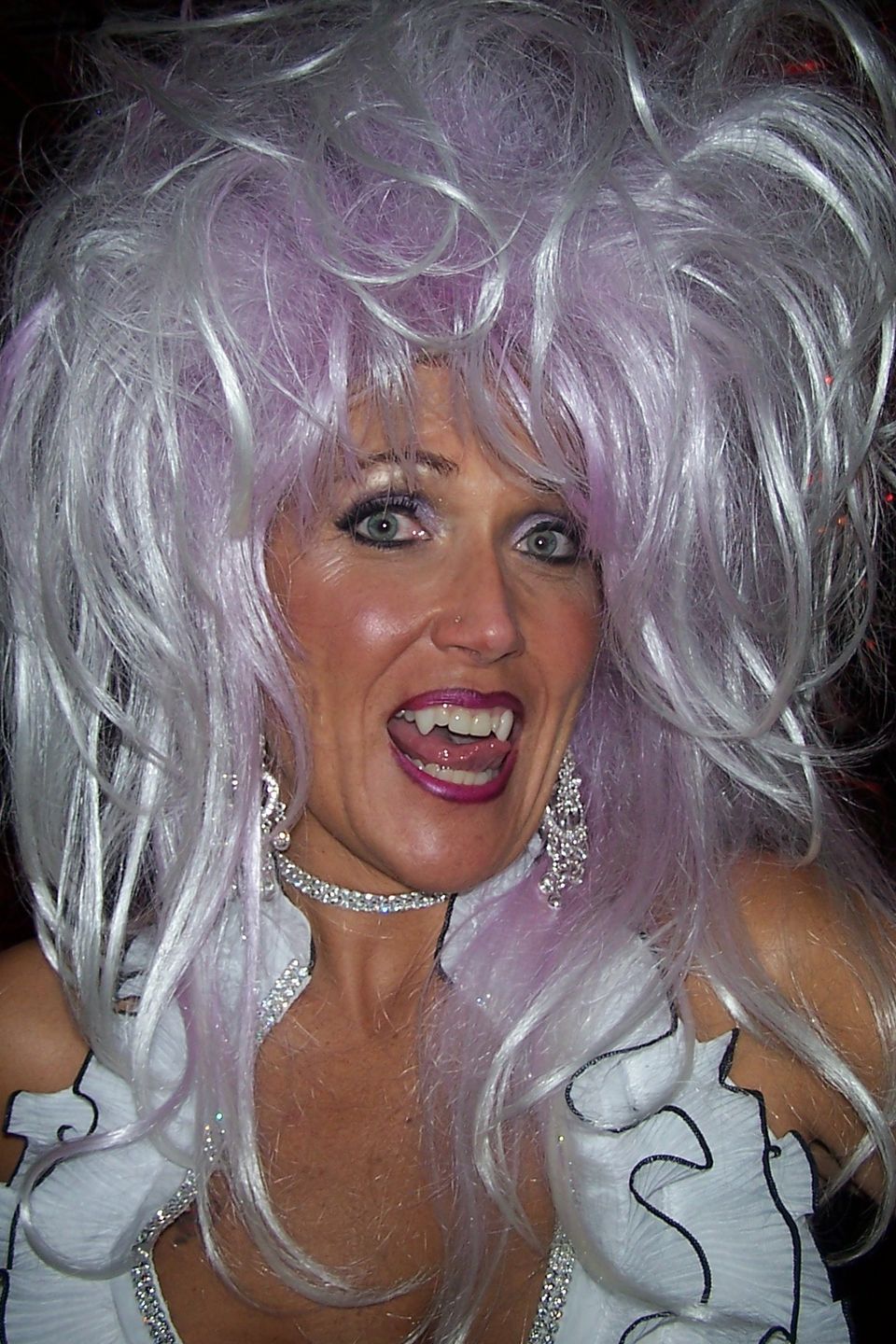 Woman wearing a large white and lavender wig at a themed event.