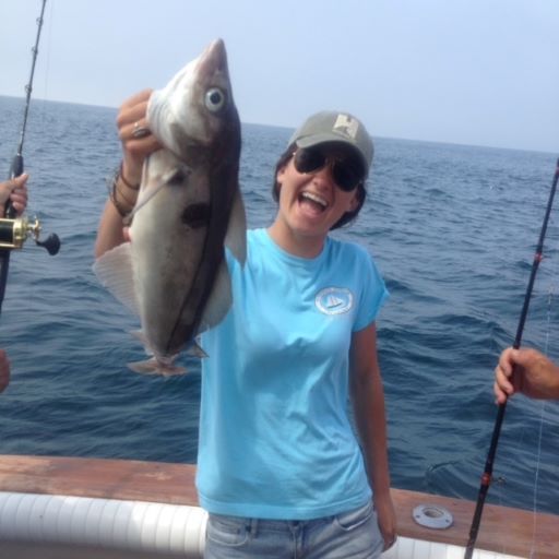 Woman wearing cap and sunglasses holding large haddock