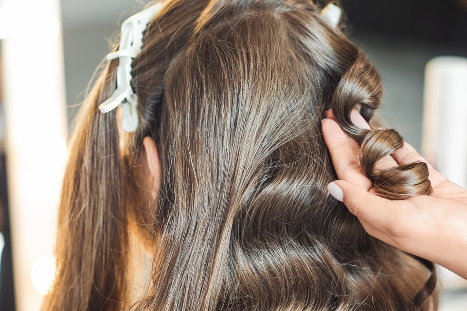 Close-up of a stylist curling and shaping a brunette wig during a professional wig styling appointment.