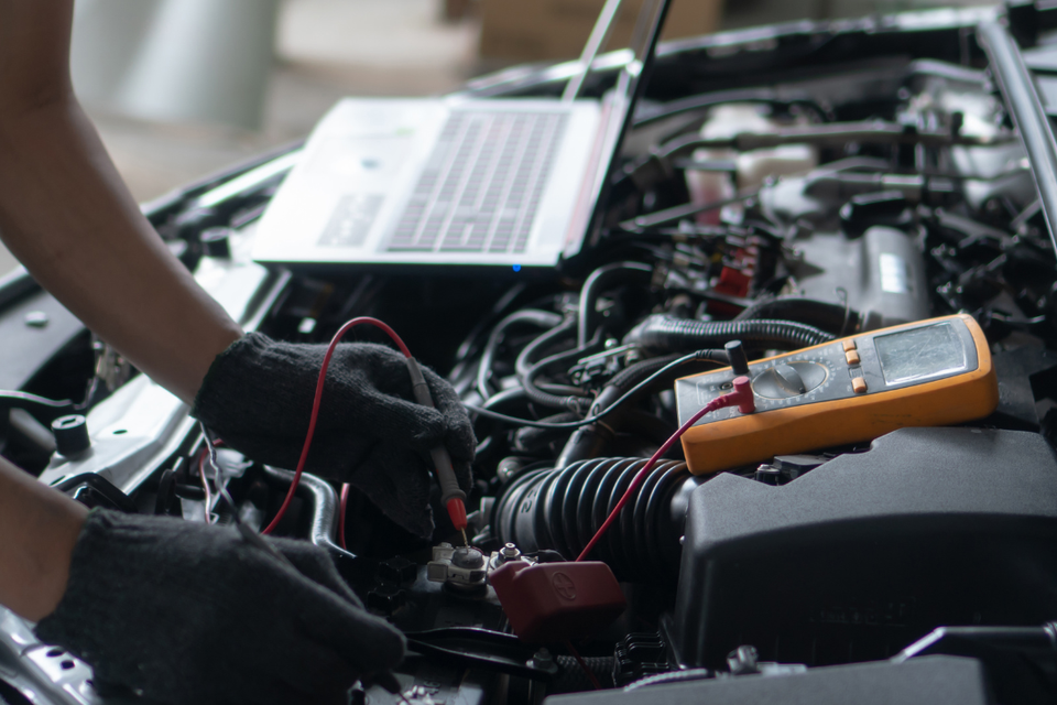 Technician performing a vehicle diagnostic test using electronic testing equipment under the hood of a car.