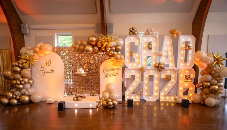 Gold balloon decor, sequin backdrop, and marquee letters styled for a 2026 graduation party