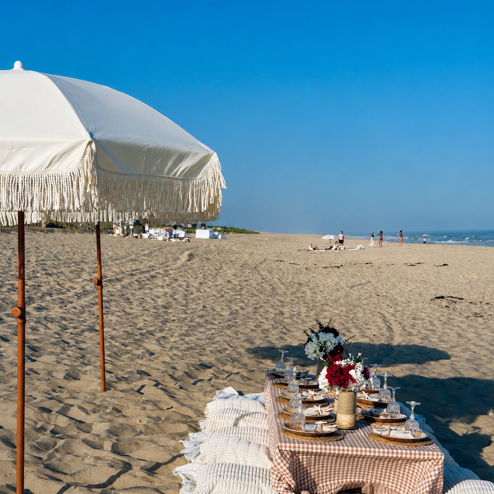 Luxury beach picnic with fringed umbrella and gingham linens styled on a Hamptons shoreline