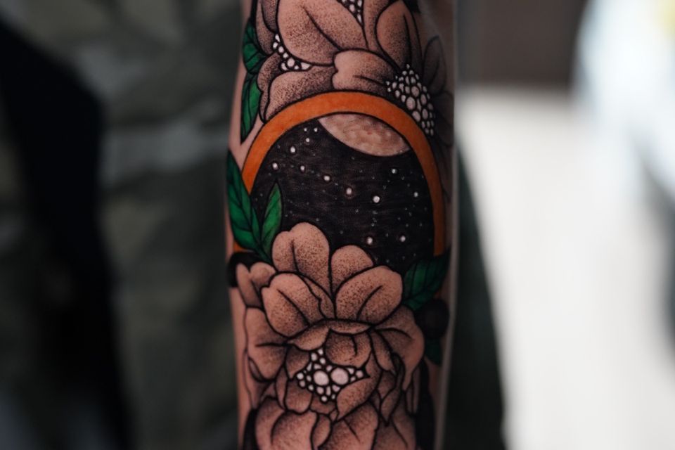 Image of a woman's forearm with a very unique and colorful tattoo in black, green, white, orange and grey