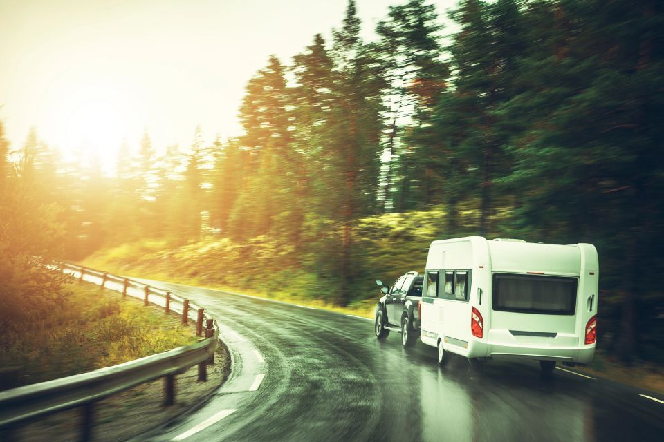 Pickup truck towing a white travel trailer on a winding wet forest road for camper and travel trailer title loans