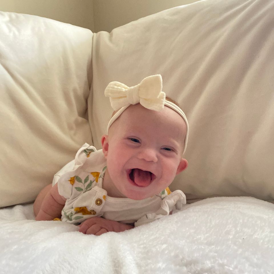 Smiling baby with Down syndrome lying on a bed, representing early support and family resources.
