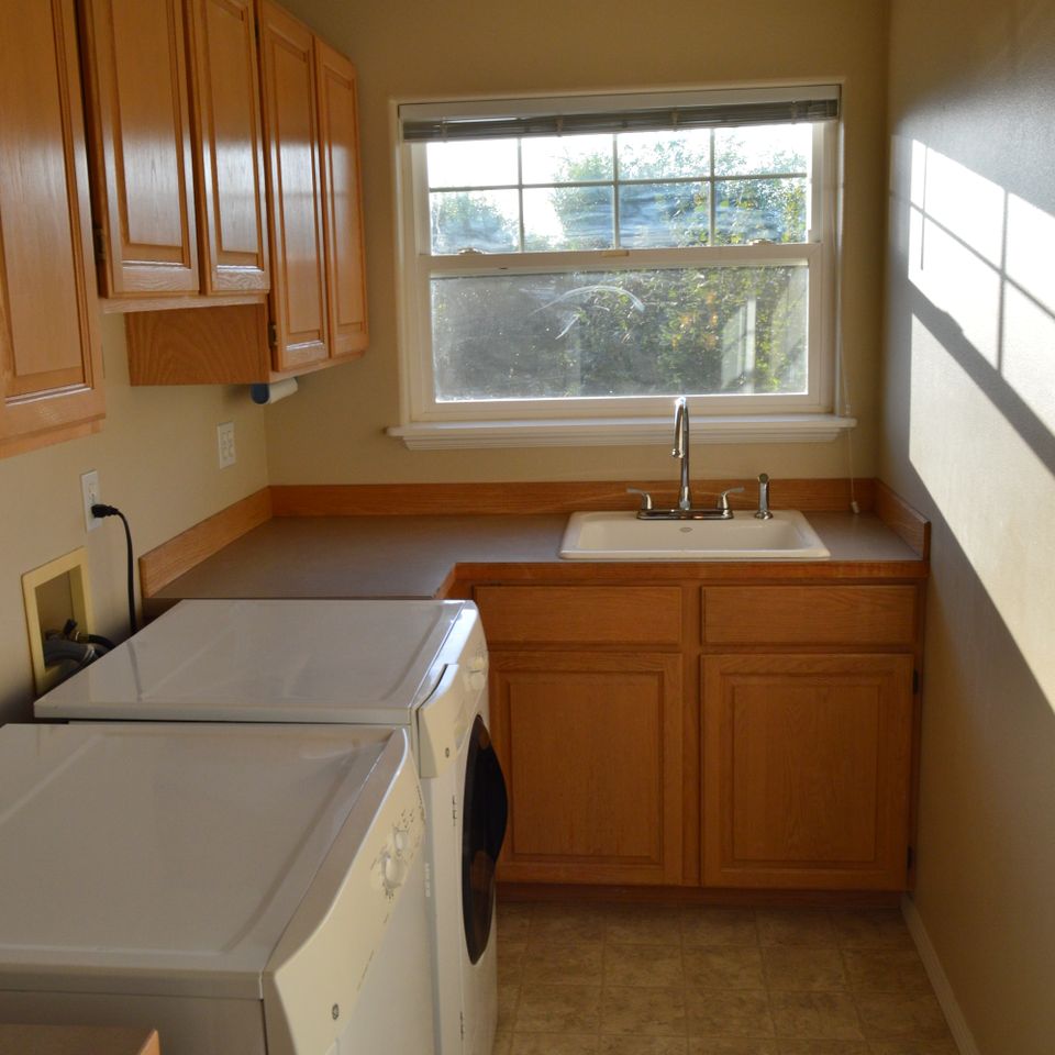 Laundry room with wood cabinets, utility sink, and washer and dryer in a custom built home