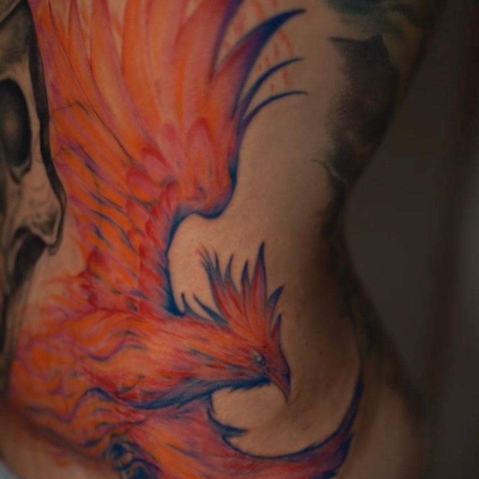 Image of an orange and read and blue phoenix in great detail tattood on the left front side of a womans body
