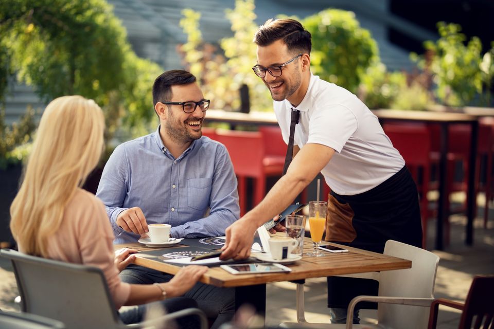 Smiling waiter serving guests restaurant preparing their table dining