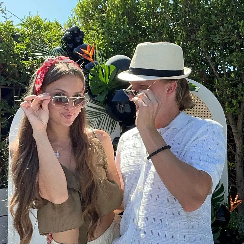 Couple wearing sunglasses and fun props while posing for a photo booth.
