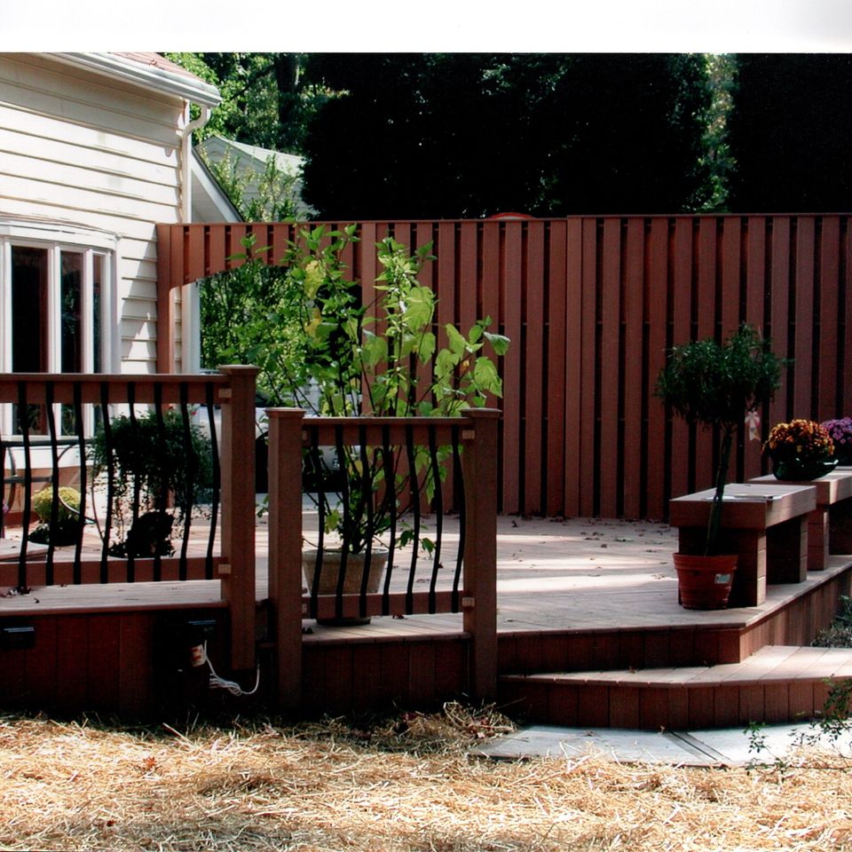 Custom backyard deck featuring built-in seating, privacy fencing, decorative planters, and multiple levels connected to a residential home.