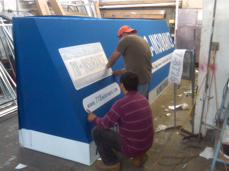 Two SignIt workers applying vinyl lettering to a large blue awning on the shop floor
