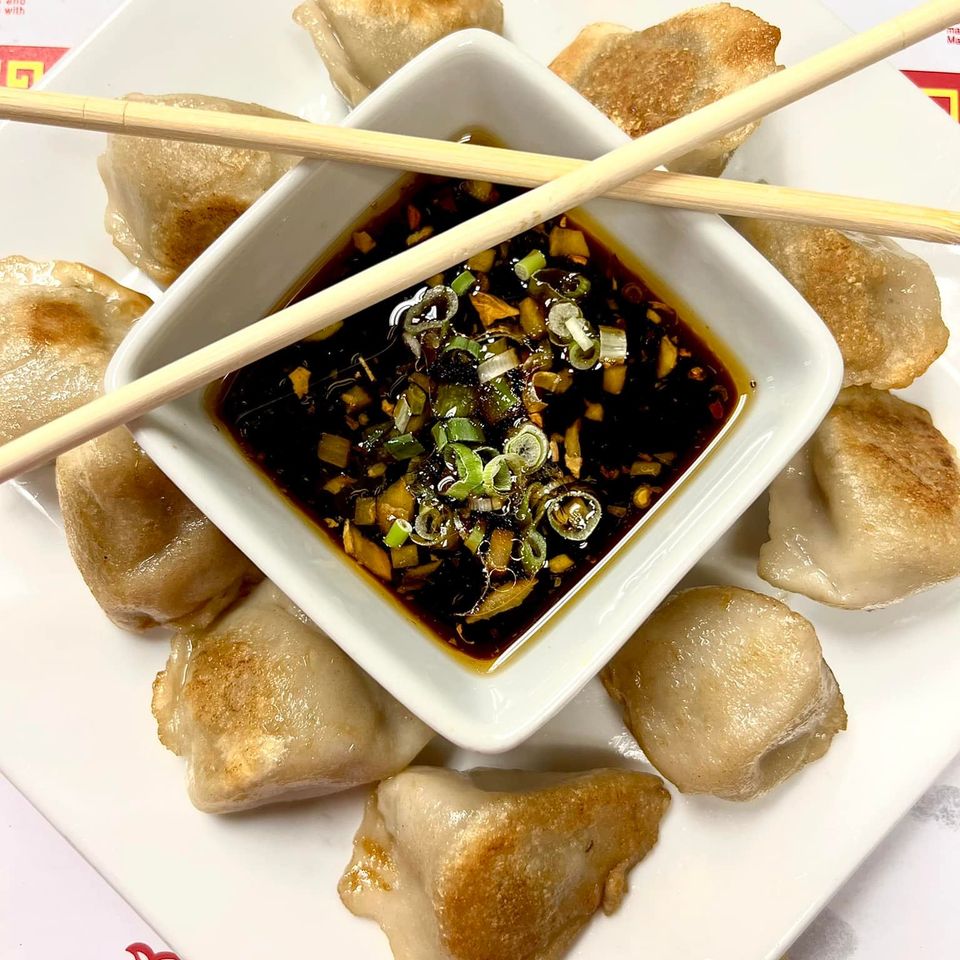 Pan-fried dumplings arranged around a bowl of savory dipping sauce.