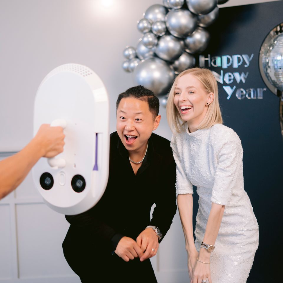 Two guests smiling and posing for a photo booth at a New Year’s party with silver balloon decorations.