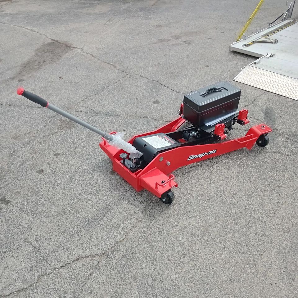 Red hydraulic floor jack used by an auto repair shop for lifting vehicles during automotive service.