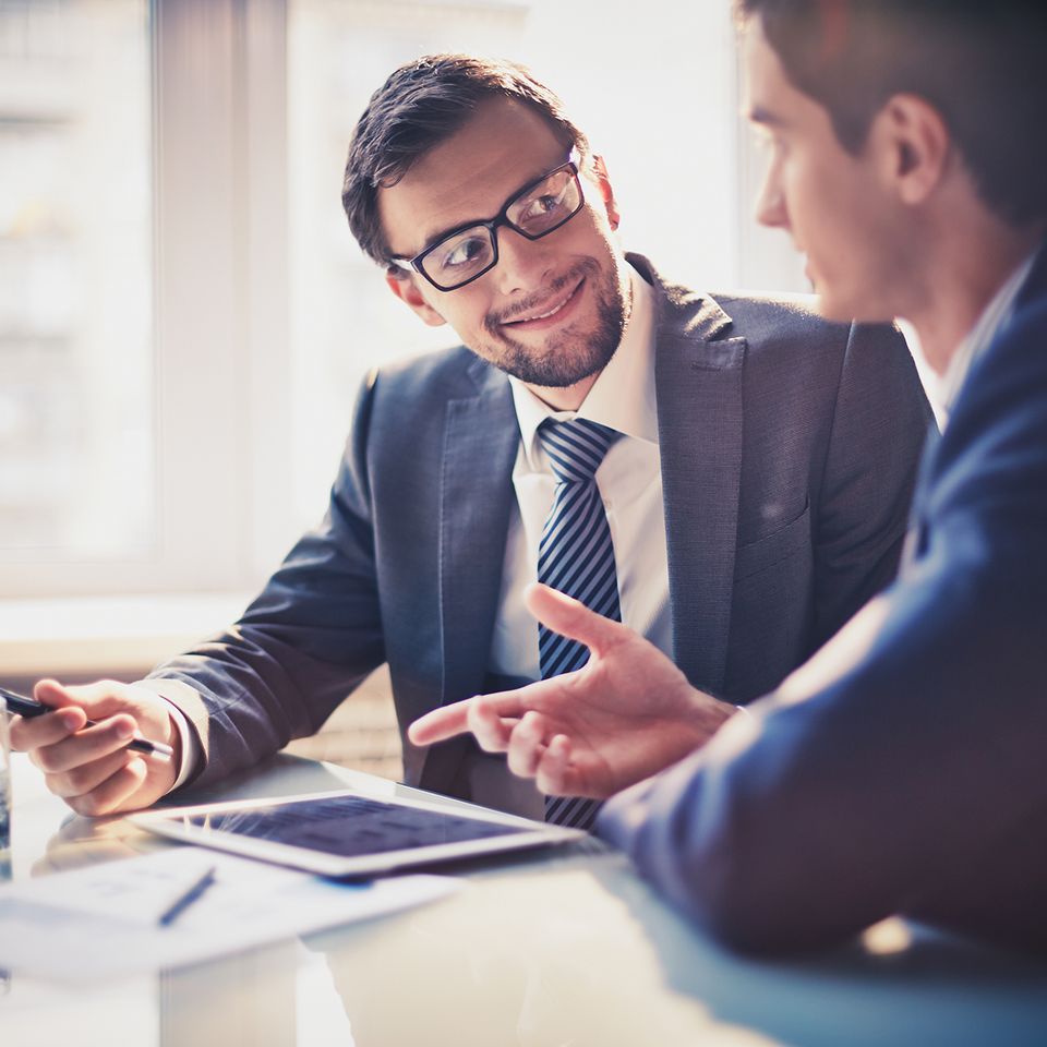Two men sitting at a desk with a tablet and discussing something