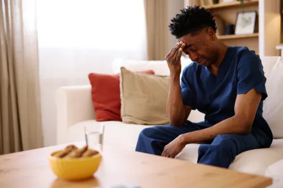 Young adult sitting on a couch holding their head  symbolizing migraine pain and treatment options.