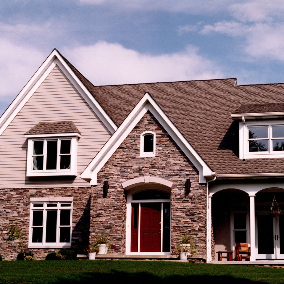 Two-story custom home with a stone and siding exterior, covered front porch, arched entryway, and professionally landscaped yard.