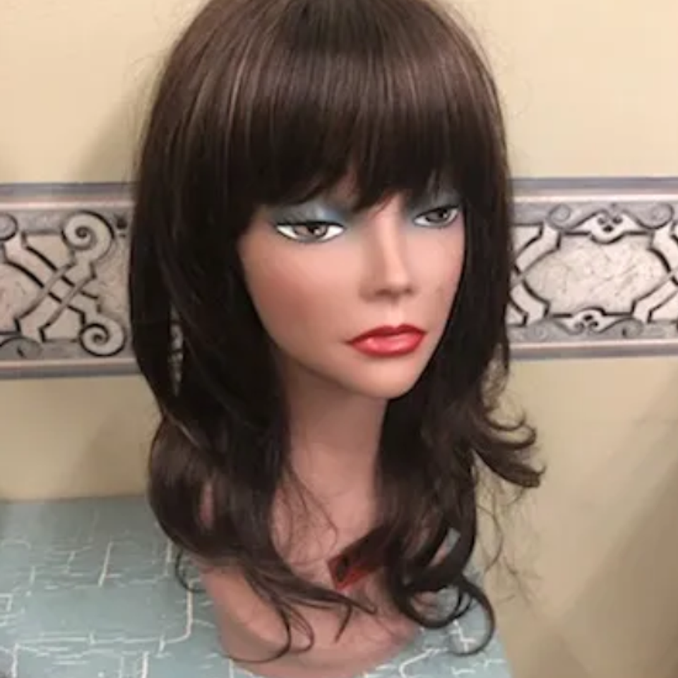 Medium-length brunette wig with bangs displayed on a mannequin, featuring soft layers and curled ends for a natural appearance.