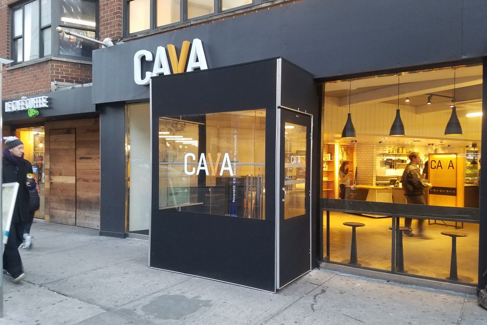 Black framed winter vestibule with a branded front panel enclosing a lit restaurant entrance on a city sidewalk