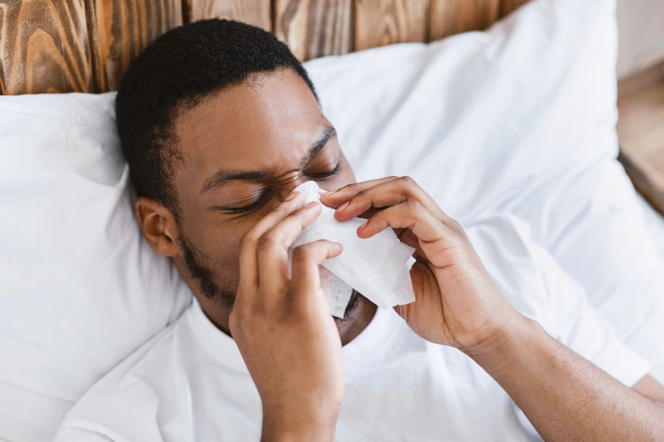 Man lying in bed blowing his nose with a tissue before Immunity IV therapy in Palm Beach County FL