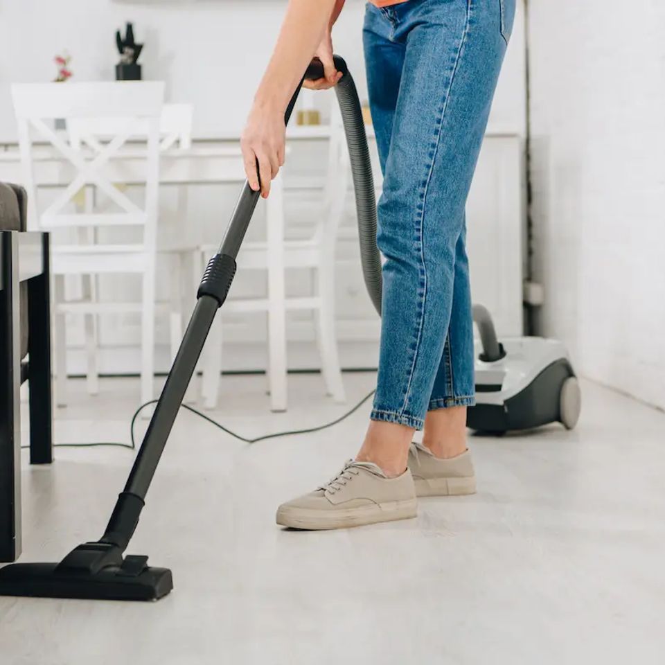 Woman vacuuming light floor in bright kitchen during house cleaning service in Virginia Beach VA