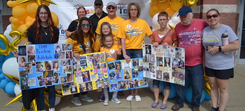 Buddy Walk team posing with photo boards in front of a DSAV balloon display and event backdrop.