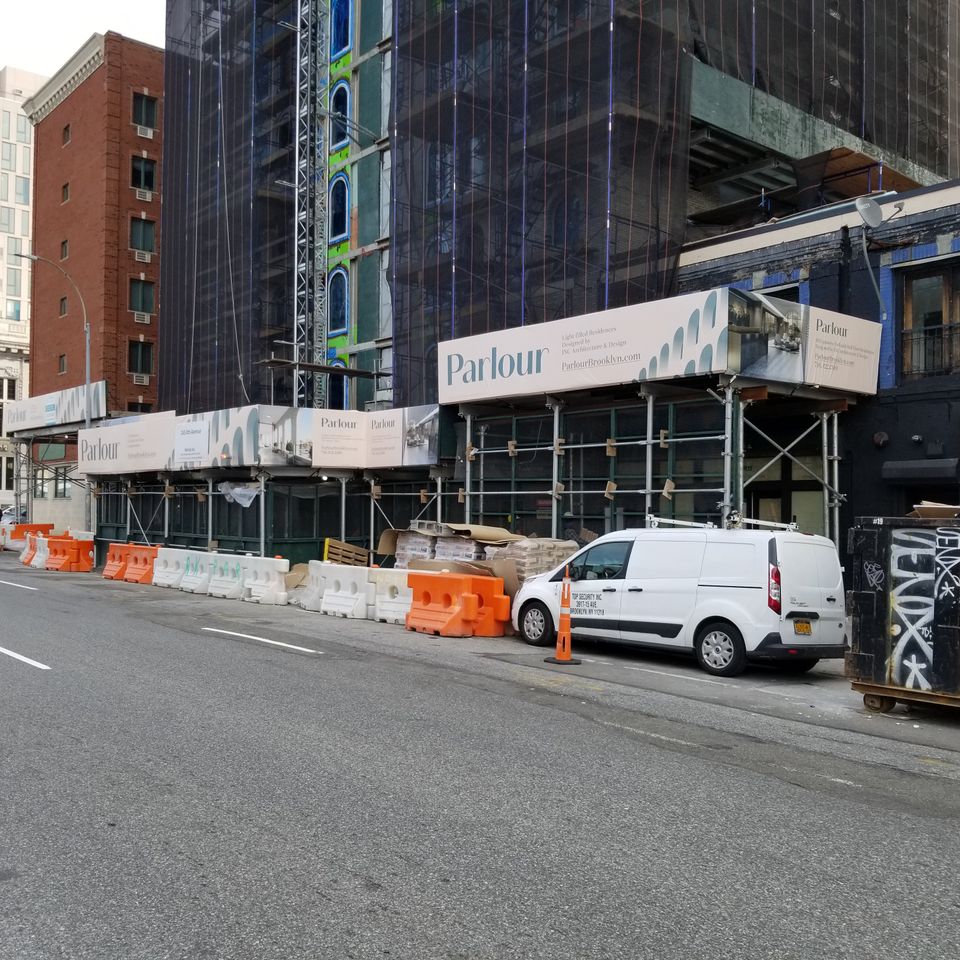 Printed banner panels wrapping a sidewalk shed on a Brooklyn corner
