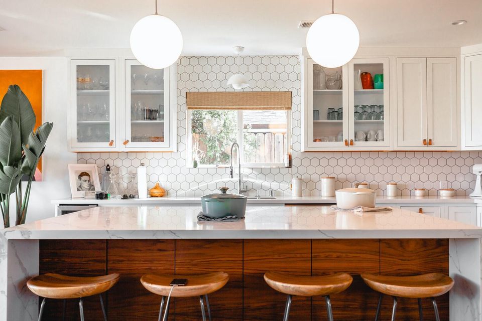 Bright modern kitchen with white marble island, wooden bar stools, hexagon tile backsplash, and natural light
