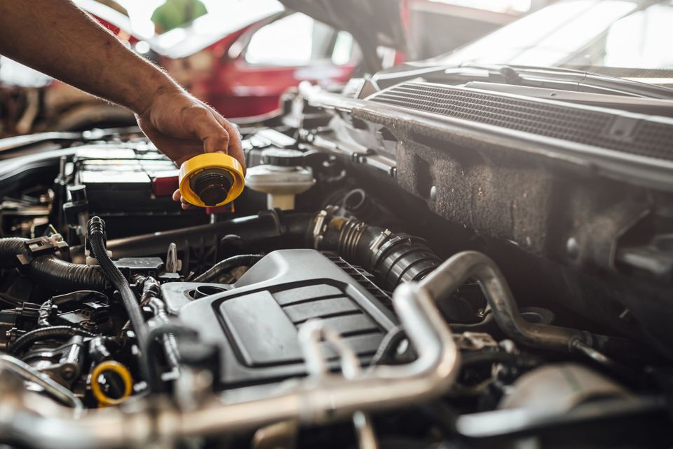 Image of a mechanic removing a cap on the motor of an automobile, brand and model unknown