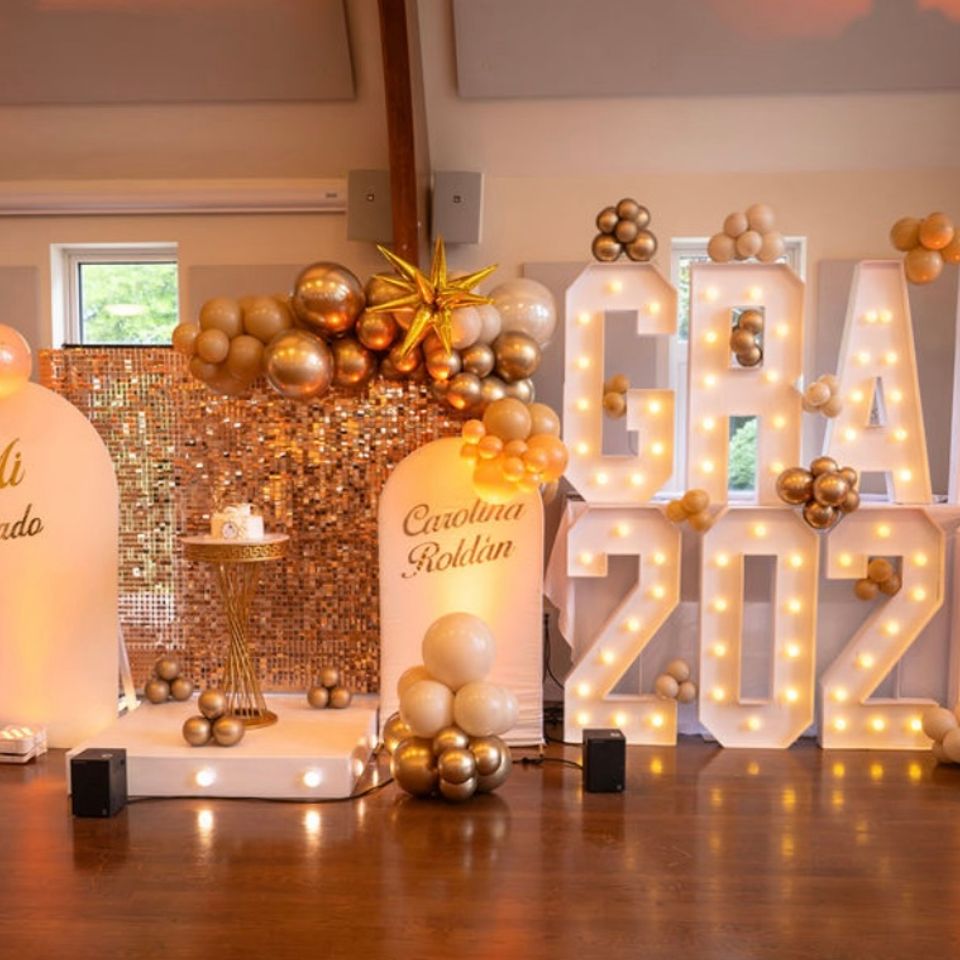 Gold balloon decor, sequin backdrop, and marquee letters styled for a 2026 graduation party