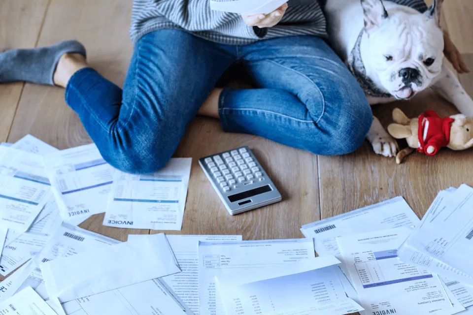 Woman sitting on wooden floor with dog and piles of bills and invoices