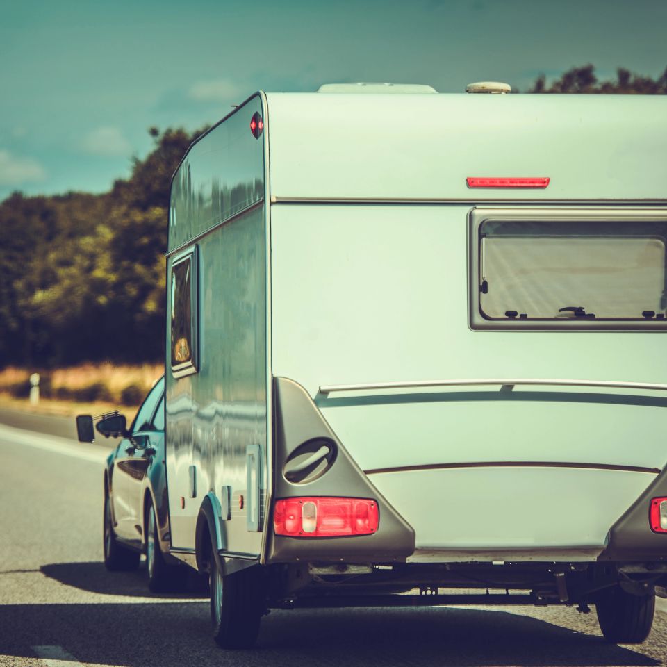 Rear view of a white camper trailer towed down a sunny highway representing travel trailer title loans