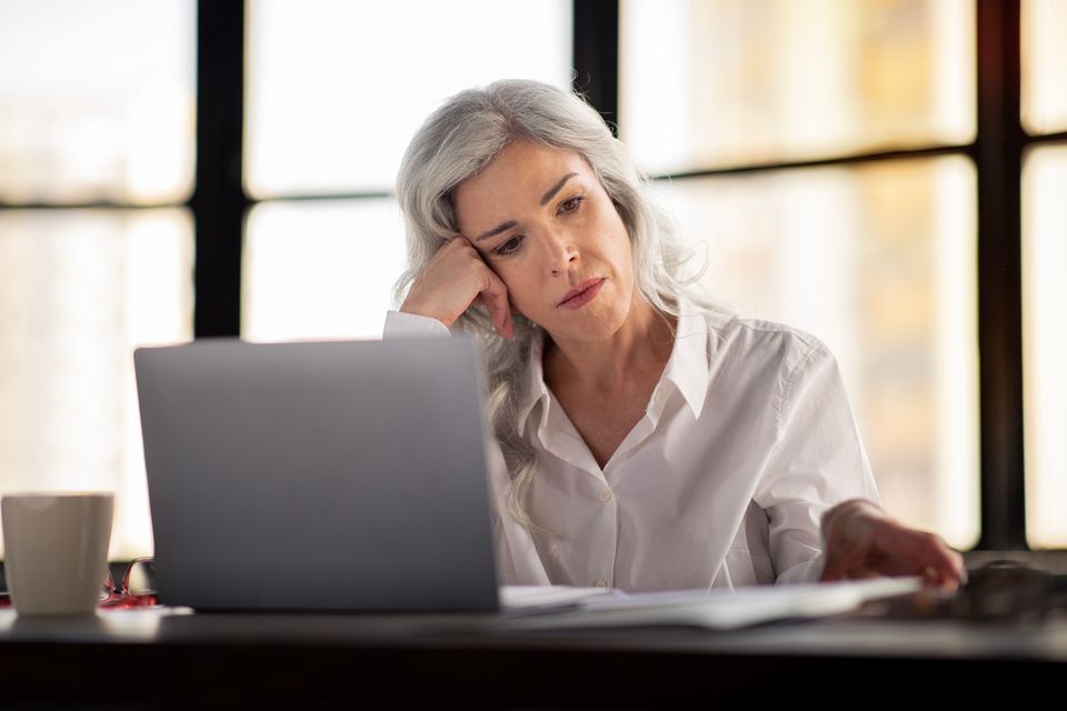 Stressed  Businesswoman Using Laptop And Looking Through Papers Working In Modern Office