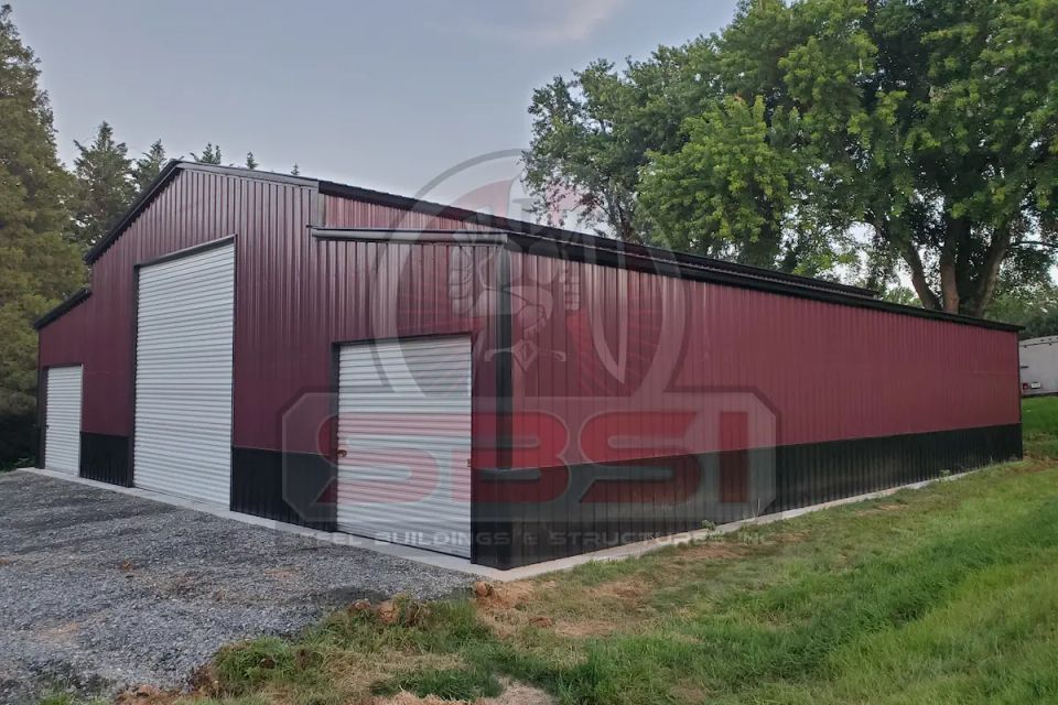 Red and black steel building with white roll up doors on gravel lot with SBSI watermark representing steel buildings in Alabama