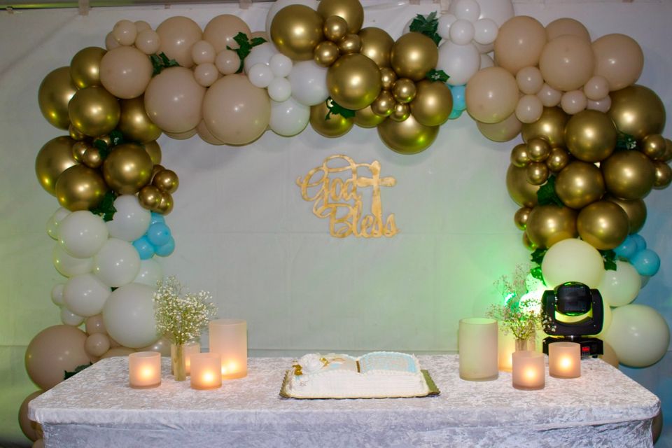 Gold and ivory balloon garland backdrop framing a cake table with candles at a celebration