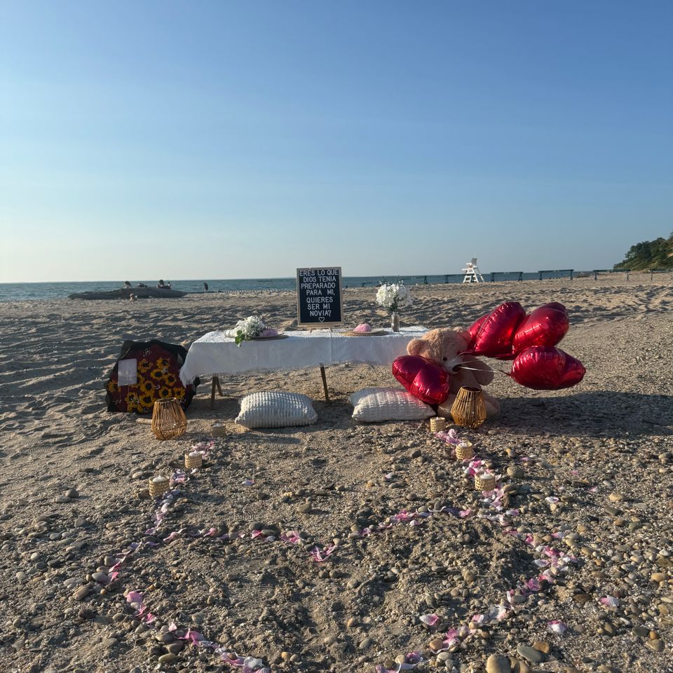 Beach proposal picnic with rose petal path, heart balloons, and candles on a Hamptons NY shoreline