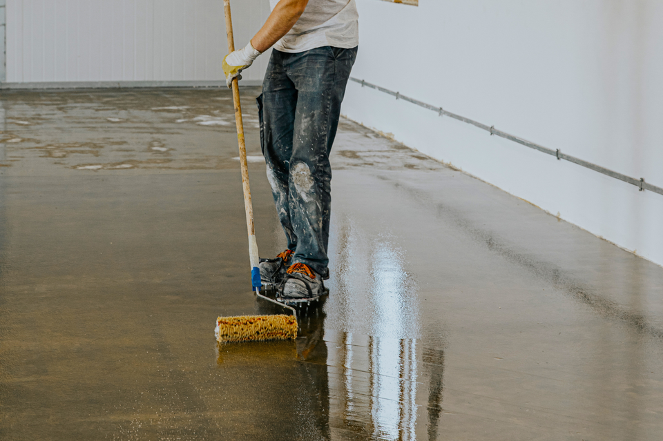 Worker applying a protective coating to a concrete floor with a roller.
